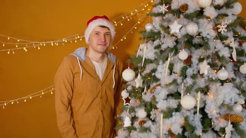 Man in Santa Hat Stands by Christmas Tree
