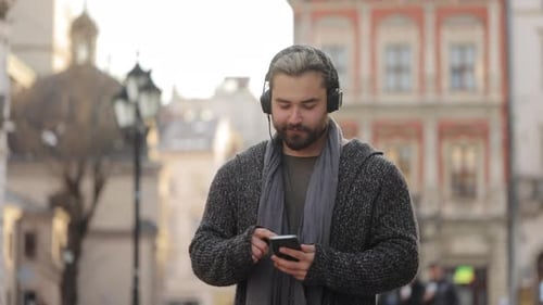 Young Man Smiling and Using Phone in City