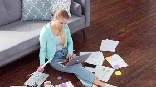 Young woman works with documents using a laptop at home.
