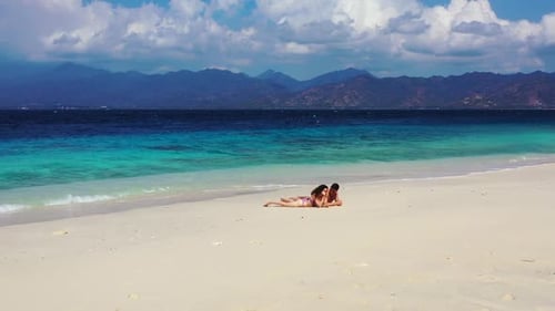 Two people sunbathing on tranquil resort beach journey by transparent ocean and white sandy backgrou