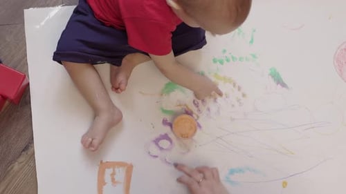 Mother and Toddler Baby Painting with Finger Paints on White Paper on Floor