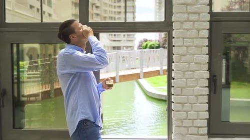 Man Standing Near Window Drinking Beverage