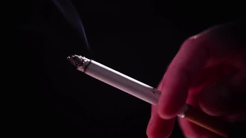Smoldering Cigarette Held in Hand Against Dark Background