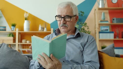 Senior Man Reading Book on Couch at Home