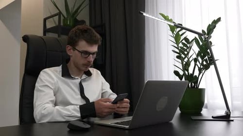 Young confident smart businessman is using smartphone sitting in his modern office desk.