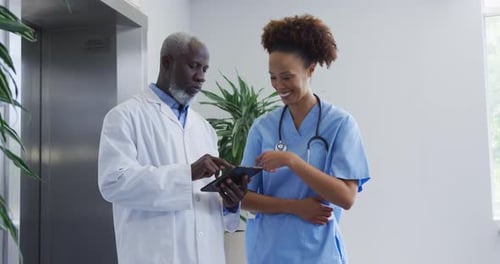 Diverse female and male doctors standing in hospital discussing over tablet