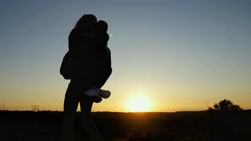 A Young Girl Jumps on Her Boyfriend and They Circle Against the Background of the Sunset a