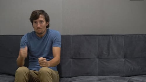 A Young Man Sits on a Couch and Feels Stress and Anger. Copy Space on the Right Side