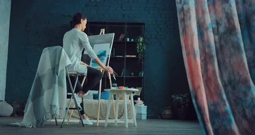 Young and Beautiful Artist Paints a Picture on Canvas in a Bright Studio