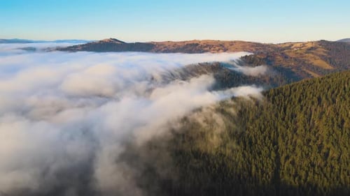 Aerial View of Landscape Above Foggy Fast Moving Clouds Covering Mountain Hills at Sunrise