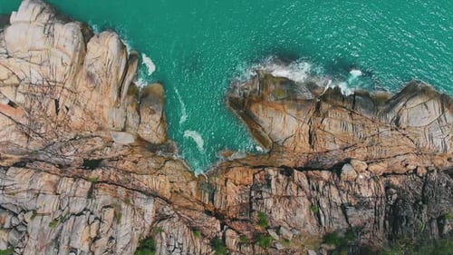 Aerial View above Waves crash on rocky cliff in Turquoise Sea on bright sunny day