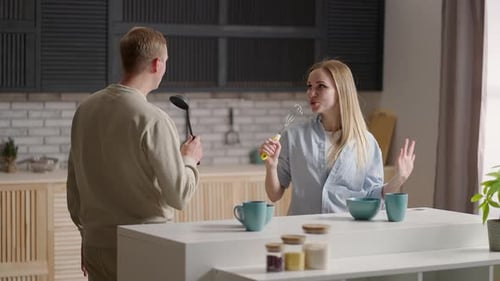 Couple Singing with Ladle and Whisk in Kitchen