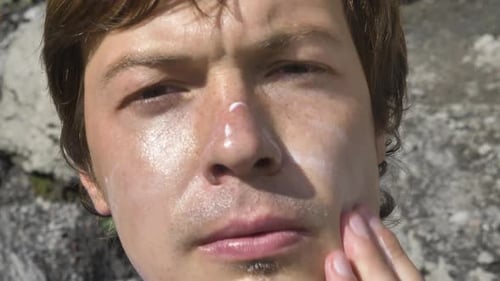 Man Puts Protection Cream with Hand to Face on Sunny Day