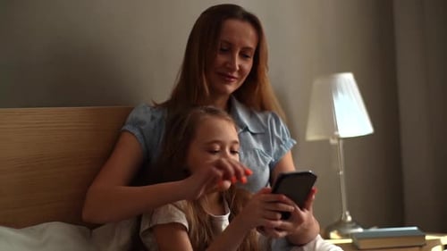 Mother and Daughter Using Smartphone Together in Bed