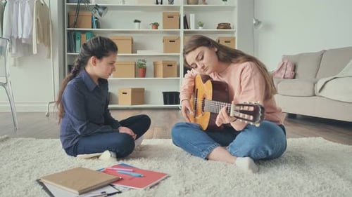 Woman Plays Guitar for Young Girl on Rug