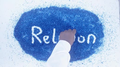 Hand Writes Word Religion Using Blue Shavings
