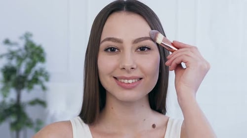 Young Woman Applies Makeup with a Brush