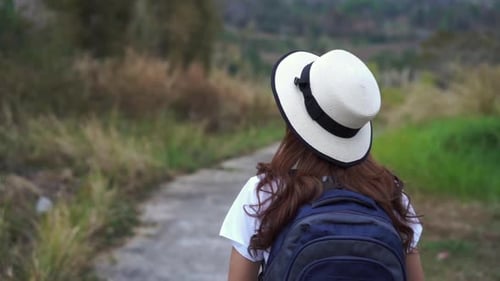 Woman Walking Along Rural Path With Backpack and Hat