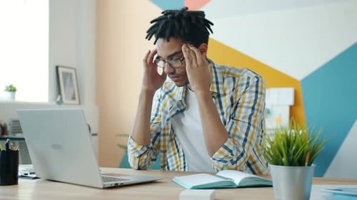 Exhausted Mixed Race Man Feeling Headache Working with Laptop in Office Room