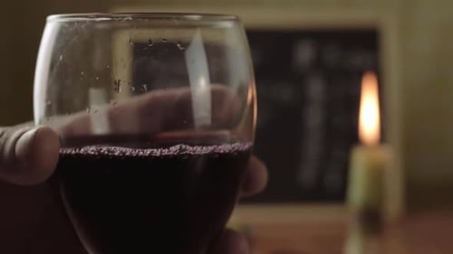 Hand holding glass of red wine with candle background close up