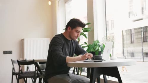 Junger Hipster-Geschäftsmann arbeitet im Café am Laptop und trinkt Kaffee