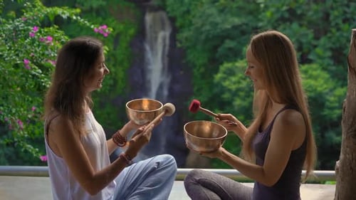 Women Playing Singing Bowls Outdoors by Waterfall