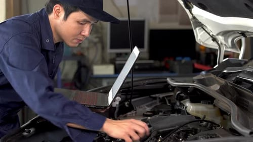 male mechanic using a laptop while repairing car in auto service