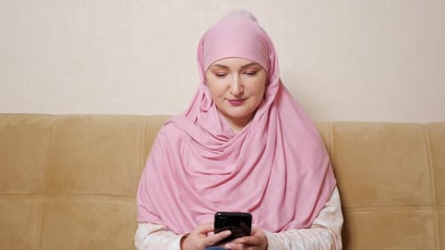 Woman in Pink Headscarf Using Mobile Phone