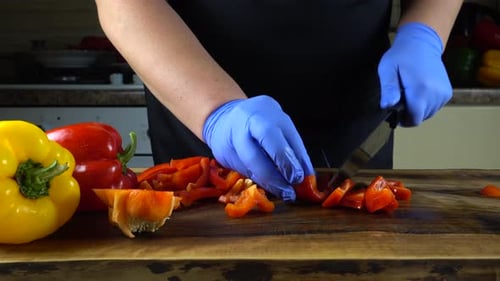 Gloved Person Dices Red Pepper with Knife on Board