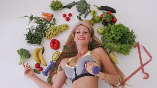 Woman with Dumbbell Lying Among Healthy Food