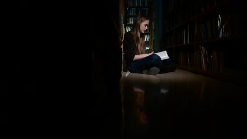 Student Girl Sitting on Floor and Examines Book in Library, Camera Moves Left To Right, Slow Motion