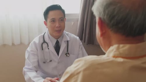 Asian male doctor taking care of senior elderly male patient sitting on wheelchair in hospital.