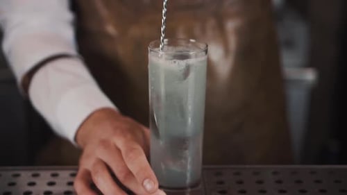 Bartender Mixing Cocktail with Spoon in Tall Glass