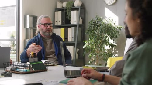 Senior Businessman Speaking with Young Diverse Team at Office Meeting