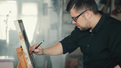 The Artist Is Working on a Painting on the Easel in the Workshop with a Pencil