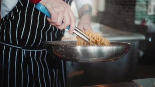 Cook Tossing Spaghetti with Tongs in Kitchen