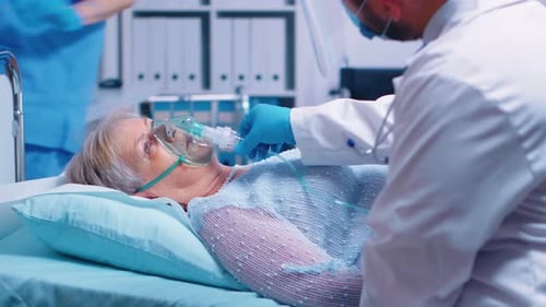 Senior Woman Lying in Hospital Bed with Oxygen Mask