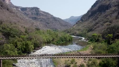 Aerial drone flying away from a suspension bridge which crosses a river in a canyon