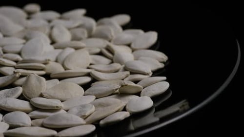 Shelled Pumpkin Seeds Rotating on Black Reflective Surface