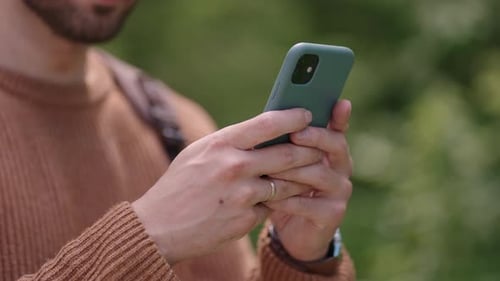 Closeup of a Mobile Phone in the Hands of a Male Traveler Walking Through the Forest