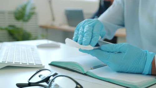 Close-up of Woman's Hands Wiping Smartphone with Sanitizer Using Tissue in Workplace