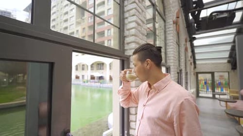 Man Drinks Coffee Near Window in Urban Cafe