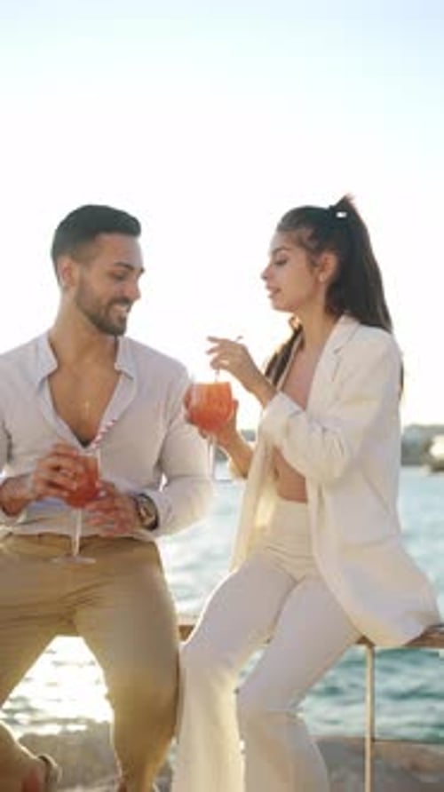 Cheerful Hispanic Couple Drinking Beverages While Speaking on Embankment
