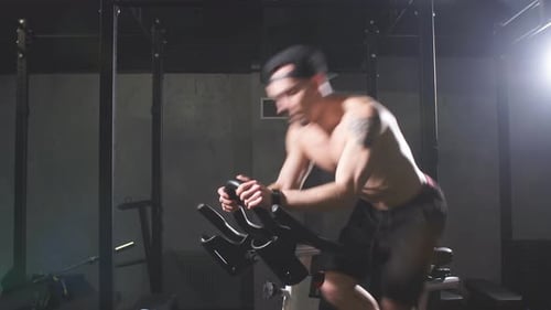 Cardio Workout. Shirtless Athletic Man Training on Cycling Machine in Gym.