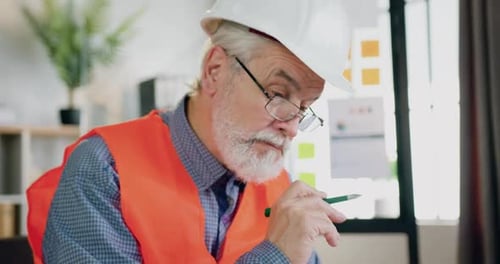 Arquitecto barbudo maduro con casco y chaleco trabajando con Blueprint