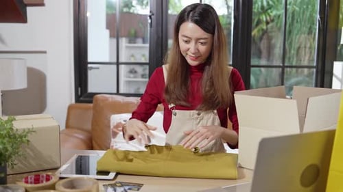 Asian female shop owner packing clothes into the box prepare to delivery