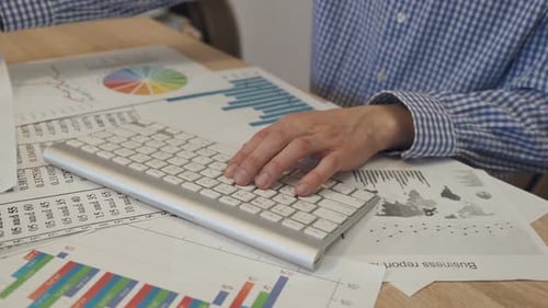 Typing at Desk Covered with Charts and Graphs