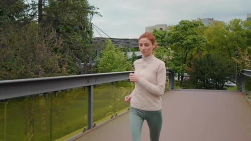 Woman Running Across Bridge in Urban Park