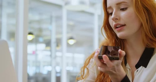 Woman Talking into Phone While Working on Laptop