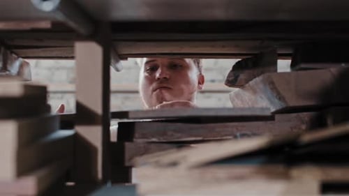 Carpentry Works a Man in a Carpentry Workshop Takes a Wooden Detail From the Shelf and Blowing Dust